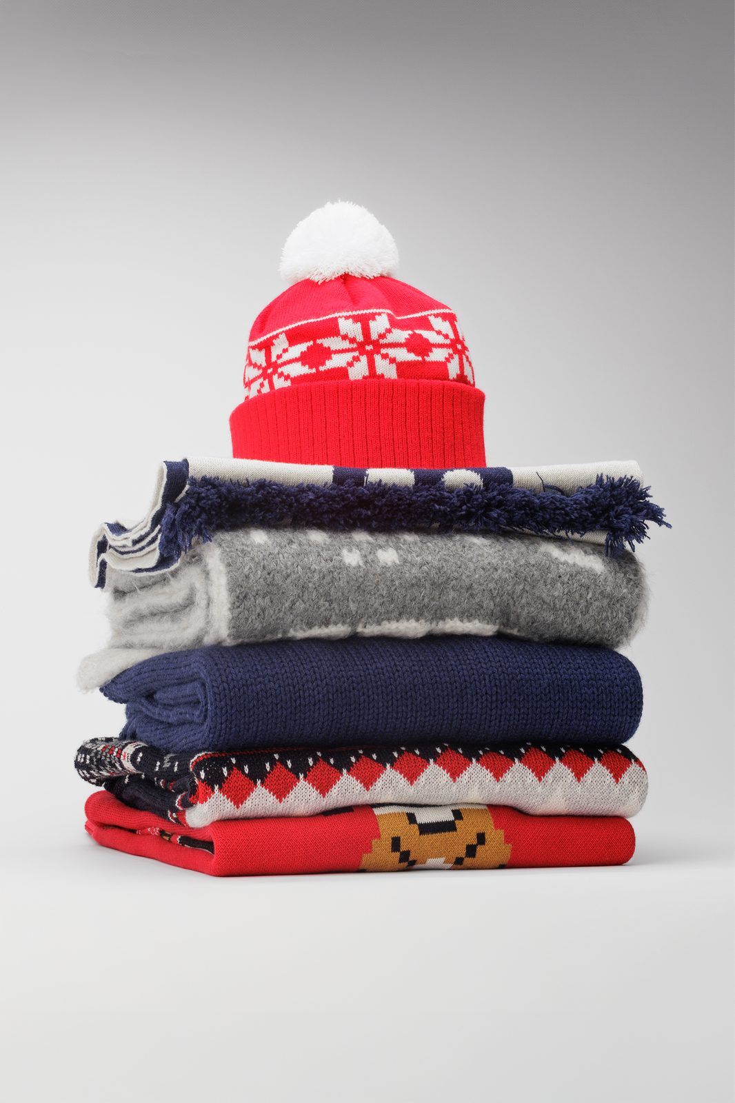 Stack of winter knitwear with a red pompom beanie